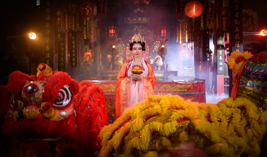 Mujer con vestimenta tipica de China, junto a unos leones chinos